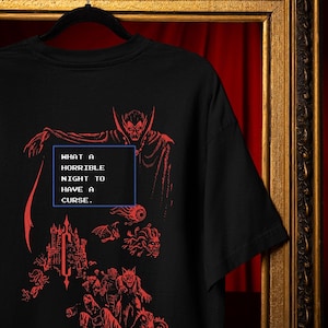 Black Comfort Colors gothic vampire shirt with red pixel horror artwork, castle, monsters, and retro game quote design.