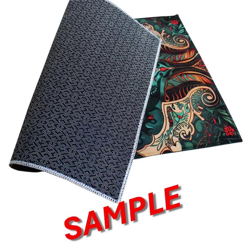 May include: A rectangular floor mat featuring a dark, intricate pattern with shades of green, orange, and red. The underside of the mat is black with a textured, non-slip geometric pattern. The word SAMPLE is printed in large red letters below.