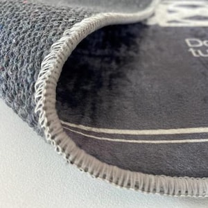 May include: Close-up of a gray rug with a white stitched edge. The rug has a white stripe across the center and the text "Don't turn your back on me" is visible in the upper right corner.