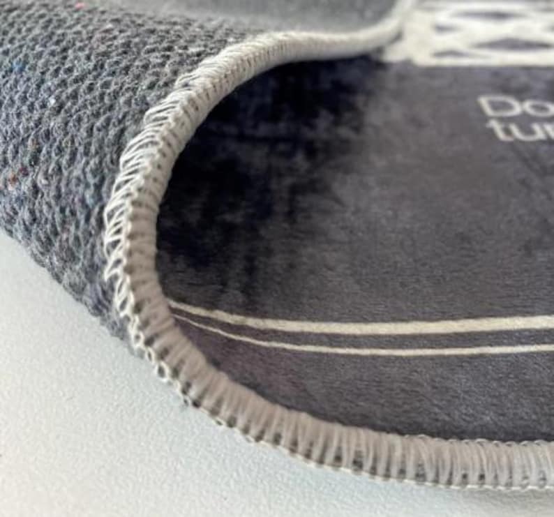 May include: Close-up of a gray rug with a white stitched edge. The rug has a white stripe across the center and the text "Don't turn your back on me" is visible in the upper right corner.