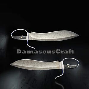 Op de afbeelding: Twee Damascus stalen messen met gebogen lemmeten en lusvormige handvatten worden getoond tegen een zwarte achtergrond. De lemmeten hebben een uniek patroon en de handvatten zijn zwart met gouden accenten. De tekst "DamascusCraft" is zichtbaar.