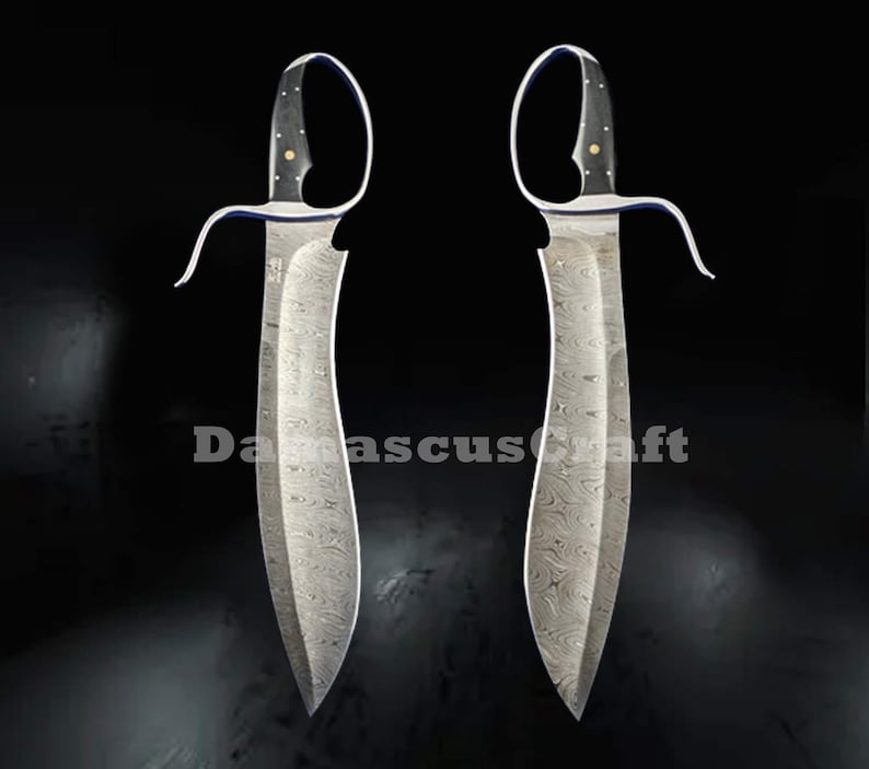 Op de afbeelding: Twee Damascus stalen messen met gebogen lemmeten en open lus handvatten. De handvatten zijn zwart met gouden accenten. De lemmeten hebben een uniek patroon. De tekst "Damascuscraft" is zichtbaar.