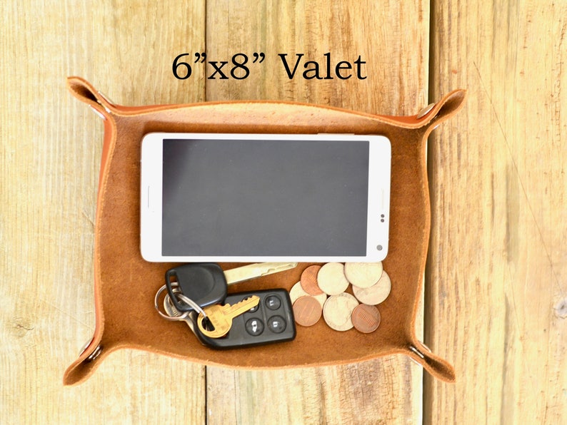 Puede incluir: Una bandeja valet de cuero marr&oacute;n con un tel&eacute;fono inteligente, llaves y monedas en su interior. La bandeja mide 15,24 cm por 20,32 cm.