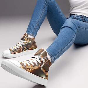 May include: White high-top sneakers with a brown and gold design. The sneakers have white laces and soles. The shoes are worn by a person wearing blue jeans and a white tank top.