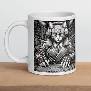 Puede incluir: Taza de cerámica blanca con una ilustración en blanco y negro de un gato con auriculares y gafas de sol, vestido con una gabardina y corbata, operando un teclado. La taza tiene un asa grande y un acabado brillante.