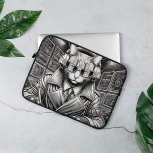 May include: Laptop sleeve featuring a cat wearing sunglasses, headphones, and a trench coat. The black and white illustration has a tech theme with computer screens in the background. The sleeve is on a white laptop.