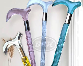 May include: Four decorative walking canes in various colors. The canes have curved handles and textured shafts. Colors include purple, blue, teal, and yellow. The handles are silver or chrome. The canes are displayed against a white background.