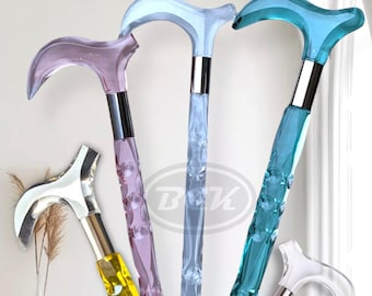 May include: An assortment of decorative walking canes in various colors. The canes feature transparent handles in shades of purple, blue, and yellow, with silver and chrome accents. The shafts have a faceted design, and the handles are curved.
