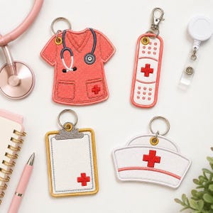 Puede incluir: Cuatro llaveros bordados con motivos médicos: una casaca de quirófano color coral con estetoscopio, una tirita blanca con cruz roja, un portapapeles blanco con cruz roja y una cofia de enfermera blanca con una cruz roja.