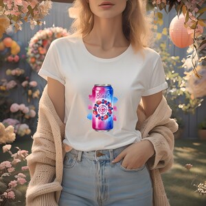May include: White t-shirt with a colourful graphic of a beverage can. The can design features the word "Blast" and a target design with berries. The shirt is paired with blue jeans and a beige cardigan.