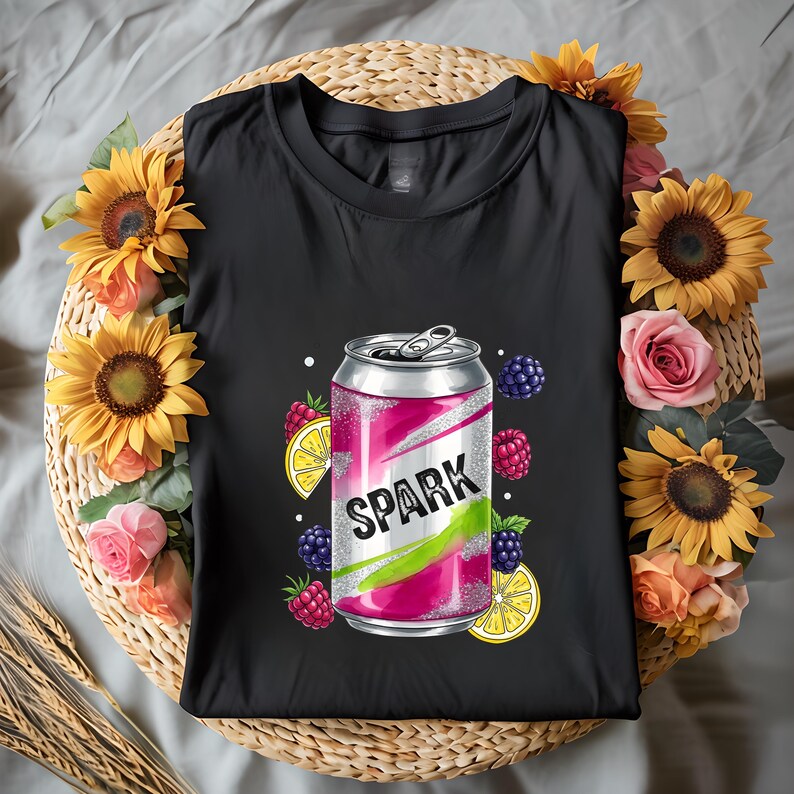 May include: Black t-shirt with a graphic of a pink and silver soda can, the word "SPARK" is printed on it. The design includes lemons, raspberries, and blackberries. The shirt is surrounded by sunflowers and roses.