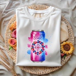 May include: White t-shirt with a graphic of a beverage can, the word "Blast" is written on it. The can design includes a target, strawberries, blueberries, and raspberries. The design has pink and blue watercolour splashes.