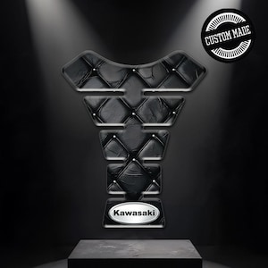 Può includere: Protezione serbatoio moto nera con design trapuntato effetto pelle e borchie argentate. Presenta un logo Kawasaki e un emblema "CUSTOM MADE". Il design è scuro ed elegante.