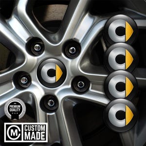 May include: A car wheel with a silver alloy rim and black wheel nuts. The centre cap displays the Smart logo: a silver "C" with a yellow arrow. Additional caps are shown. The image also includes a "Custom Made" logo.