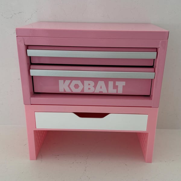 May include: A pink metal tool chest with two drawers featuring silver handles and the white text KOBALT printed on the front. Below the metal chest is a separate pink stand with a single white drawer and an open storage space at the bottom.