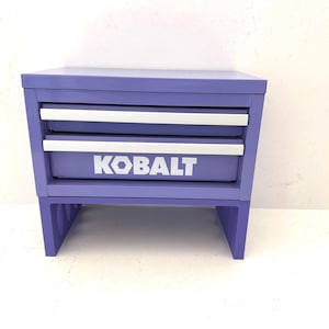 May include: A purple tool chest with two drawers and the word "KOBALT" in white. The chest has a rectangular shape and is elevated on short legs.