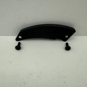May include: A black, curved metal piece with two screw holes and two black screws. The metal piece has a textured surface and a matte finish. The screws are positioned below the metal piece.