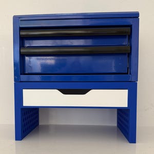 May include: A blue metal tool chest with a white drawer and black drawer pulls. The chest has a glossy finish and is designed to sit on a workbench. The bottom of the chest has a perforated design.