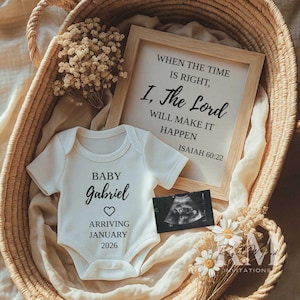 May include: A white baby onesie with the name "Gabriel" and the arrival date of January 2026, placed in a woven basket with a framed sign that reads "When the time is right, I, The Lord will make it happen Isaiah 60:22".