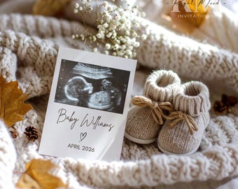 Könnte beinhalten: Eine Schwangerschaftsankündigung mit Ultraschallbild und Babyschuhen. Die Karte trägt die Aufschrift "Baby Williams" mit einem Herz und "April 2026". Die beigefarbenen Strickschuhe haben braune Schleifen und liegen auf einer cremefarbenen Strickdecke.