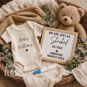 May include: A cream-colored ribbed baby bodysuit with the text Baby Williams and a heart, a square letter board reading WE ARE JUST AS Shocked AS YOU! ARRIVING MARCH 202X, a brown teddy bear, a pregnancy test, and greenery in a woven basket.