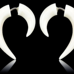 May include: A pair of white, curved earrings with a horn-like design. The earrings have a smooth, polished surface and a silver-colored connector. The background is black, with a reflection of the earrings below.