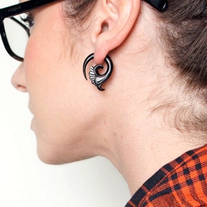 May include: A black spiral ear gauge with a decorative design. The gauge is worn in a person's ear.