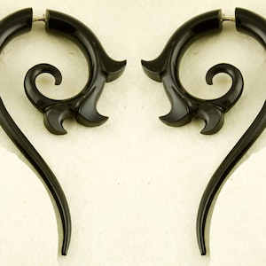 May include: A pair of black, decorative earrings. Each earring has a curved, elongated shape with a swirling central detail and a flared, petal-like design. The earrings are made of a glossy material.