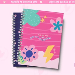 May include: Two spiral bound notebooks with colorful covers. The front cover of the pink notebook features a yellow lightning bolt, a pink flower with a blue center, and the text "Naz que hoy sea un dia especial". The back cover of the blue notebook has a white floral pattern.