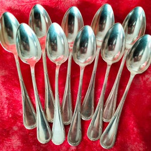 May include: Ten silver teaspoons with ornate handles. The spoons are arranged in a semi-circle on a red velvet surface.