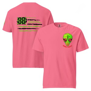 May include: Two pink t-shirts with a graphic design. The back of one shirt features a green, black and white American flag with alien heads. The front of the other shirt features a green alien head with red X's over its eyes and the text "SEEK TRUTH".