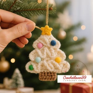 May include: Cream-colored crocheted Christmas tree ornament with colorful pom-poms and a yellow star on top. The tree has a brown crocheted base and is suspended by a gold string. The text "Crochetlover99 + Crochet Shop" is visible.