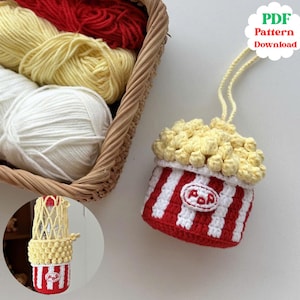 May include: A handmade crochet popcorn-shaped item with red and white stripes, topped with yellow popcorn. The item has a small "POP" label and a string for hanging. A basket of yarn in red, yellow, and white is in the background. The image also includes a small, round image of the popcorn item.