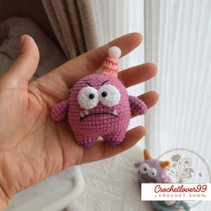 Pu&ograve; includere: Un giocattolo mostro fatto a mano, all'uncinetto in tonalit&agrave; di rosa e viola. Il giocattolo ha grandi occhi bianchi, un'espressione scontrosa e un cappello da festa. Il giocattolo &egrave; alto circa 7.6 cm.