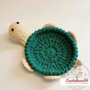Puede incluir: Una tortuga de ganchillo hecha a mano en tonos verdes, beige y crema. La tortuga tiene un caparazón texturizado, una cabeza beige con ojos negros y aletas beige. El logotipo de Crochetlover99 está en la esquina inferior derecha.