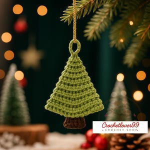Könnte beinhalten: Handgefertigter grüner Häkel-Weihnachtsbaumschmuck mit braunem Stamm, der an einem goldenen Faden hängt. Der Baum hängt vor einem verschwommenen Hintergrund mit Weihnachtsbeleuchtung und einem kleinen Baum. Der Shop-Name "Crochetlover99" ist sichtbar.