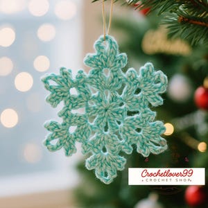 May include: A crocheted snowflake ornament in shades of teal and white hangs from a gold string. The snowflake is in focus, with a blurred background of a Christmas tree and soft lights. The ornament is handmade and has a delicate, openwork design.