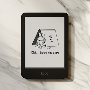 May include: Black Kobo e-reader with a white screen displaying a cartoon rabbit reading a book with headphones. The text "Shh... busy reading" is below the illustration. The Kobo logo is at the bottom.