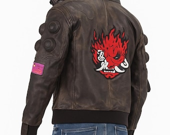 May include: Brown leather jacket with the word "SAMURAI" on the collar. The back features a red and white graphic design. The jacket has multiple pockets and a black ribbed hem. The model is wearing blue jeans.