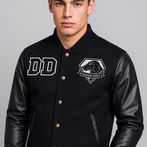 May include: Black varsity jacket with black leather sleeves. The jacket has the white letters "DD" on the chest and a "Diamon Dogs" logo patch. Gold-coloured buttons and a ribbed hem complete the design.