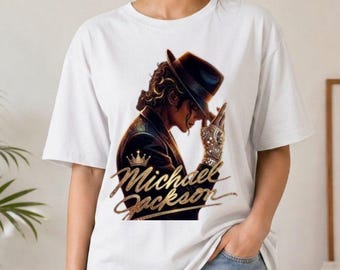 Könnte beinhalten: Weißes T-Shirt mit einer gold-braunen Grafik von Michael Jackson in einem schwarzen Hut und einer Jacke, mit dem Namen "Michael Jackson" in goldener Schrift. Das Design beinhaltet eine Krone und einen detaillierten Handschuh.