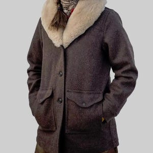 May include: A brown wool coat with a cream-colored shearling collar. The coat has two front pockets, a button closure, and a classic design. This outerwear piece is suitable for cold weather.
