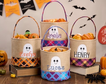 May include: Four Halloween burlap baskets with handles, each filled with pumpkins and festive items. Each basket features a ghost applique and a name. The baskets have plaid fabric accents in orange, purple, and blue.