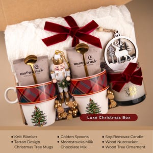 Peut inclure: Coffret cadeau de No&euml;l avec une couverture en tricot blanc, des tasses &agrave; motif tartan avec des sapins de No&euml;l, des cuill&egrave;res dor&eacute;es et du chocolat au lait Moonstrucks. Comprend une bougie en cire de soja, un casse-noisette en bois et une d&eacute;coration d'arbre en bois.