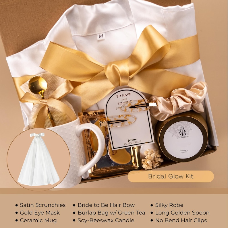 May include: A gift box with a white silky robe, gold ribbon, and a ceramic mug. The box includes a gold eye mask, soy-beeswax candle, and hair accessories. The text "Bridal Glow Kit" is visible.