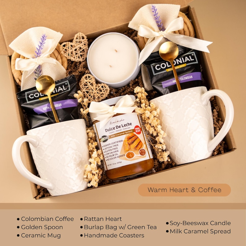 May include: A gift box with coffee, mugs, and treats. The box contains two white ceramic mugs, coffee packets with gold spoons, a candle, and a jar of dulce de leche. The box is decorated with burlap bags, rattan hearts, and handmade coasters. Text on the box reads "Warm Heart & Coffee."