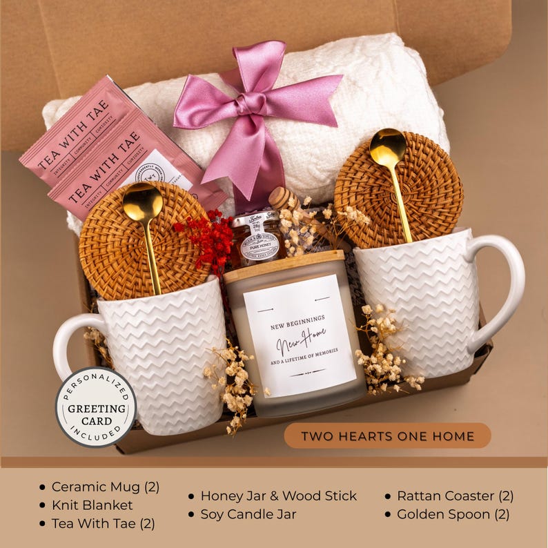 Peut inclure: Un coffret cadeau avec une couverture en tricot blanche, deux tasses en c&eacute;ramique blanches, des sachets de th&eacute;, une bougie de soja, un pot de miel, des dessous de verre en rotin et des cuill&egrave;res dor&eacute;es. La bougie indique "New Beginnings, New Home, and a lifetime of memories."