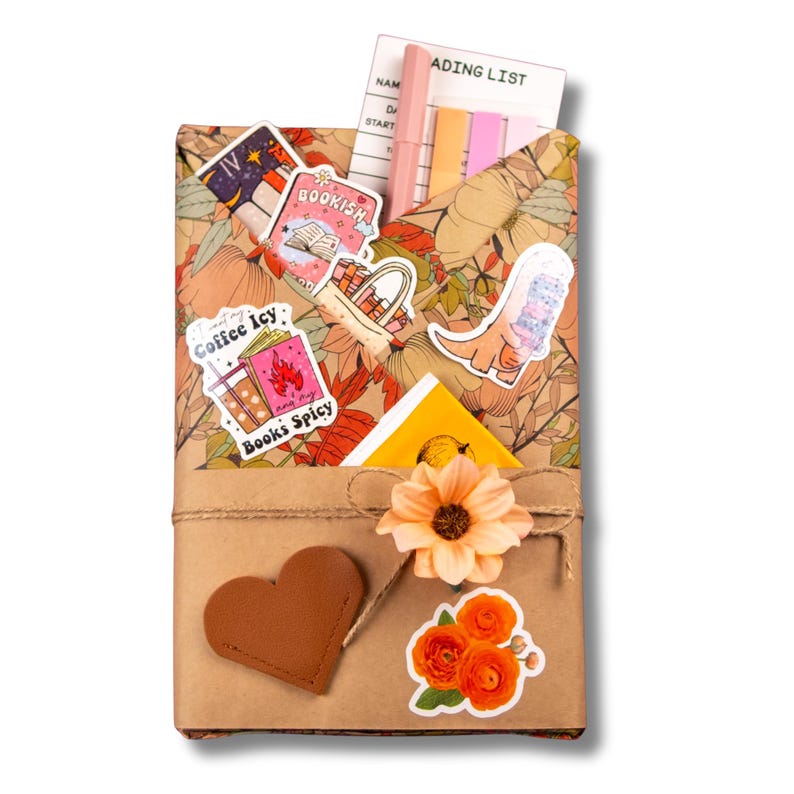 Peut inclure: Un livre emball&eacute; avec un motif floral, orn&eacute; d'autocollants, d'un patch en forme de c&oelig;ur et de fleurs orange. Le livre contient une liste de lecture, un stylo et des notes autocollantes. Les autocollants ont le texte "Bookish", "Coffee Icy Books Spicy".