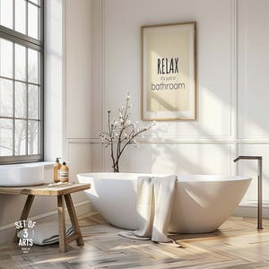 Puede incluir: Un baño luminoso y moderno con una bañera blanca de forma ovalada y un cartel enmarcado que dice "RELAX, it's just a bathroom". Un banco de madera sostiene un lavabo y artículos de tocador. Una toalla cuelga sobre la bañera.