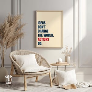 以下が含まれることがあります： 「IDEAS DON'T CHANGE THE WORLD. ACTIONS DO.」とネイビーと赤で書かれたフレームプリント。織りの椅子と白いクッションの上にプリントが飾られています。小さなサイドテーブルと装飾的な花瓶も画像にあります。